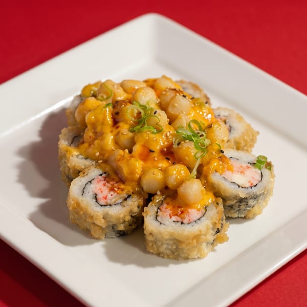 Fried sushi rolls topped with scallops, orange sauce, sesame seeds, and green onions on a white plate.