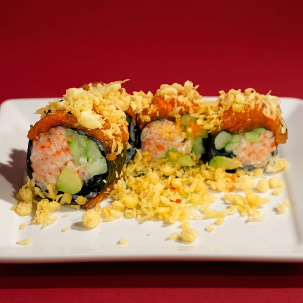 Three sushi rolls with orange sauce and crispy toppings on a white plate against a red background.