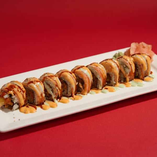 A white rectangular plate holds a row of sushi rolls with sauces and pickled ginger on a red background.